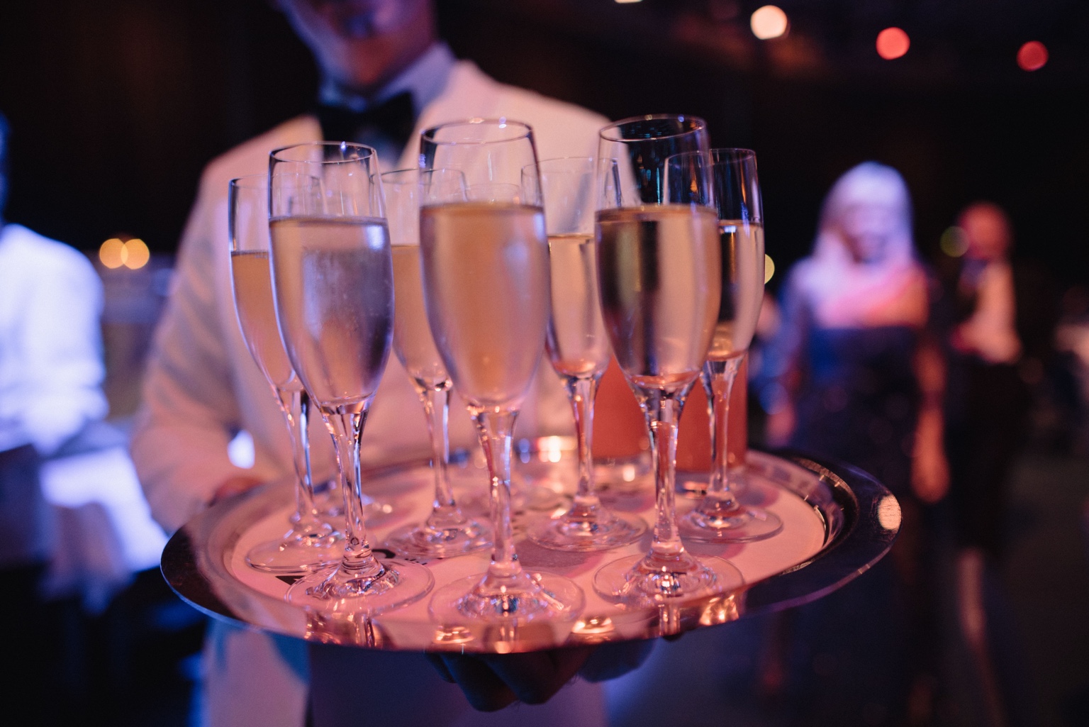 A server carrying a tray of champagne glasses at an evening reception.