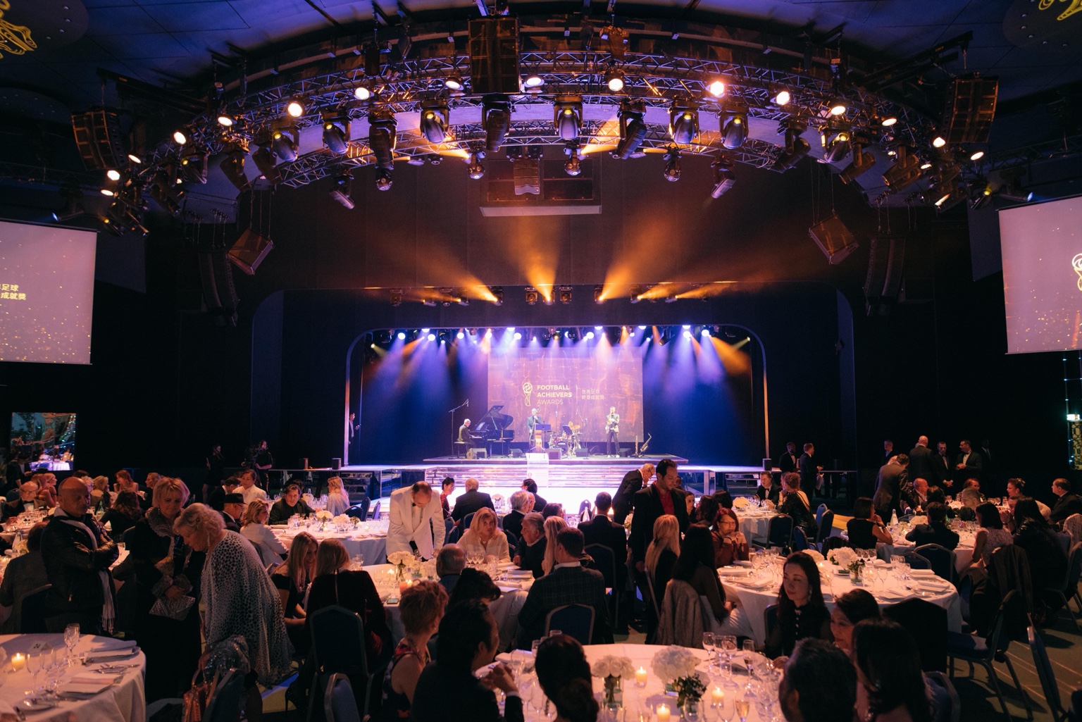Guests at dinner tables facing a lit stage and live performers.