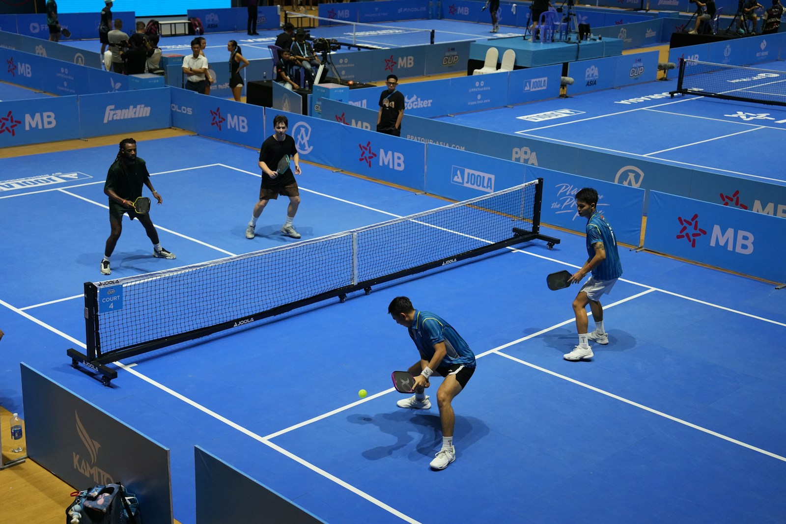 Four adults playing doubles pickleball on a blue indoor court.