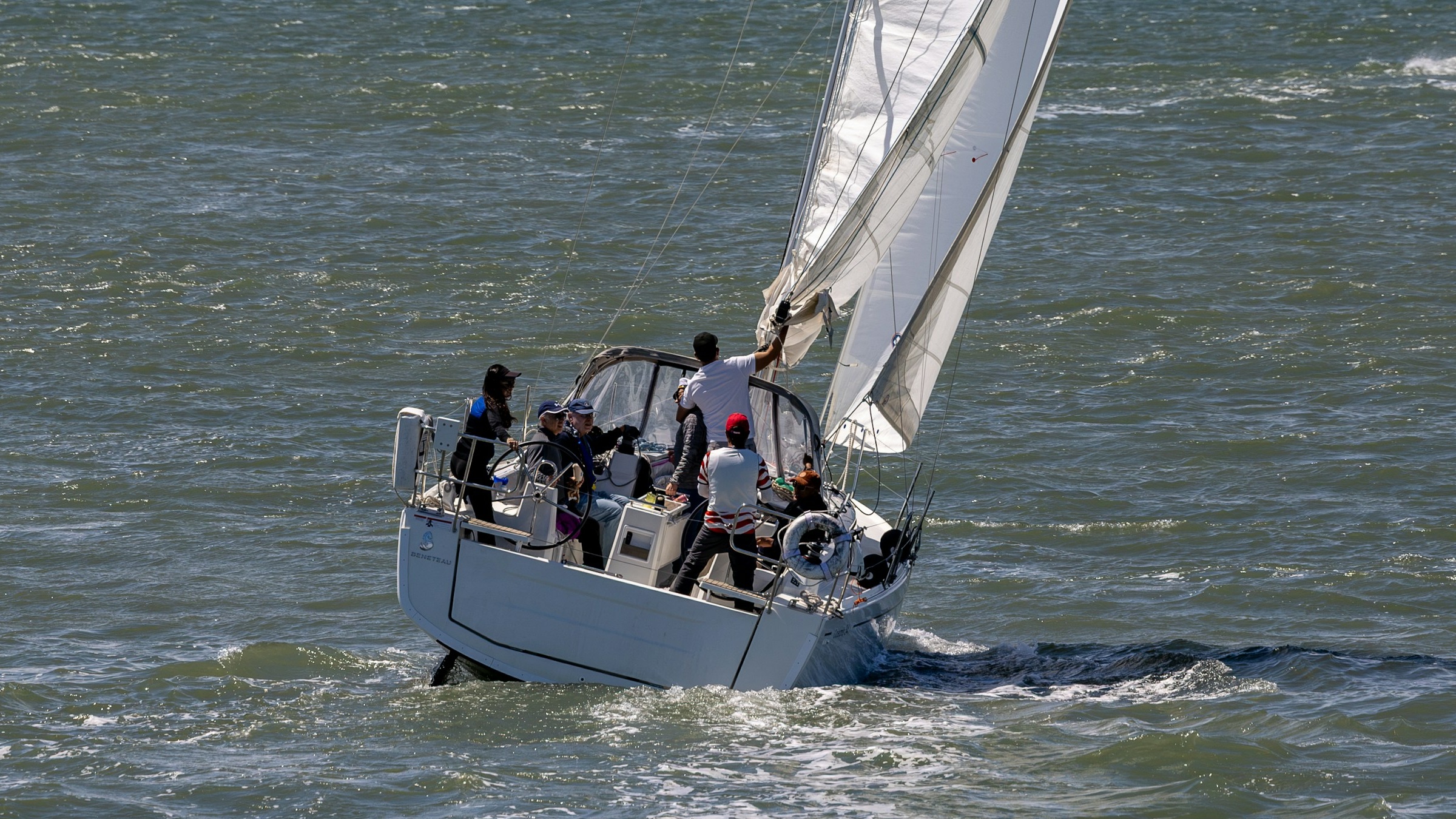 People aboard a white sailboat, with one person reaching toward the sail and others gathered around the cockpit.